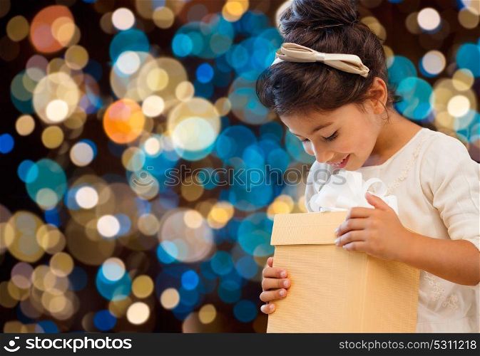 holidays, childhood and people concept - smiling little girl with gift box over lights background. smiling little girl with gift box over lights