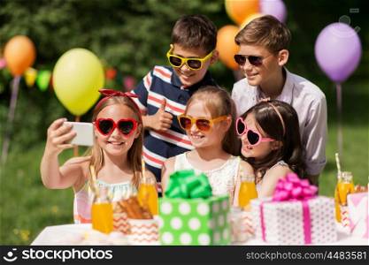 holidays, childhood and technology concept - happy kids in sunglasses taking selfie by smartphone on birthday party at summer garden. happy kids taking selfie on birthday party. happy kids taking selfie on birthday party