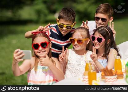 holidays, childhood and technology concept - happy kids in sunglasses taking selfie on birthday party at summer garden. happy kids taking selfie on birthday party. happy kids taking selfie on birthday party