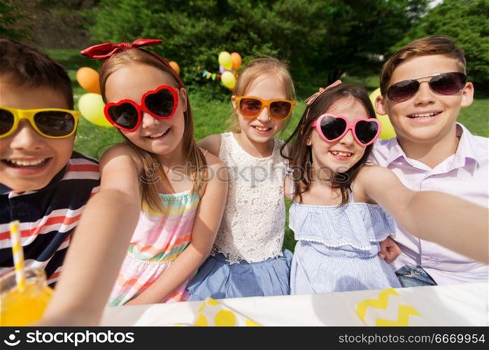 holidays, childhood and technology concept - happy kids in sunglasses taking selfie on birthday party at summer garden. happy kids taking selfie on birthday party. happy kids taking selfie on birthday party