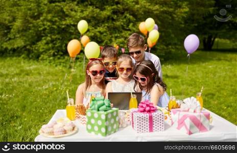 holidays, childhood and technology concept - happy kids in sunglasses with tablet pc on birthday party at summer garden. happy kids with tablet pc on birthday party