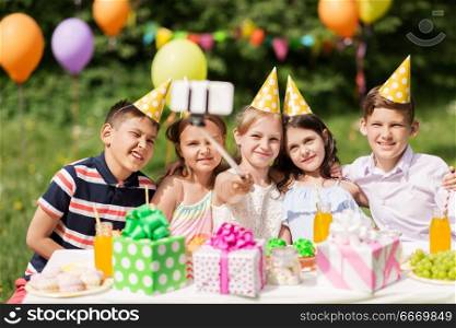 holidays, childhood and technology concept - happy kids taking picture by selfie stick on birthday party at summer garden. happy kids taking selfie on birthday party. happy kids taking selfie on birthday party