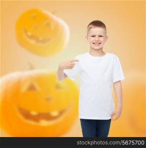 holidays, childhood, happiness, gesture and people concept - smiling little boy in white blank shirt pointing finger at himself over halloween pumpkins background