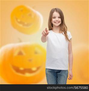 holidays, childhood, happiness, gesture and people concept - smiling little girl in white blank shirt pointing finger at you over halloween pumpkins background
