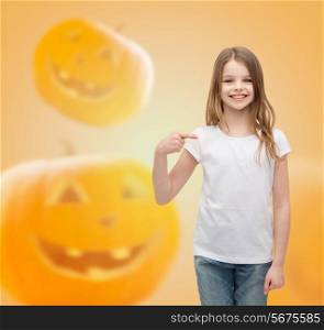 holidays, childhood, happiness, gesture and people concept - smiling little girl in white blank shirt pointing finger at herself over halloween pumpkins background