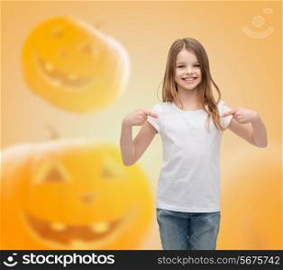 holidays, childhood, happiness, gesture and people concept - smiling little girl in white blank shirt pointing fingers at herself over halloween pumpkins background