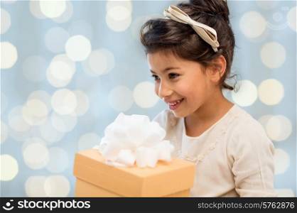 holidays, children, christmas, people and birthday concept - happy little girl with gift box over lights background