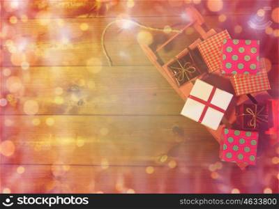 holidays, christmas, advertisement, new year and celebration concept - close up of many little gift boxes on red wooden sleigh over lights