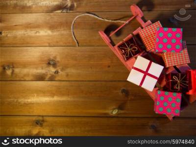 holidays, christmas, advertisement, new year and celebration concept - close up of many little gift boxes on red wooden sleigh on wooden board