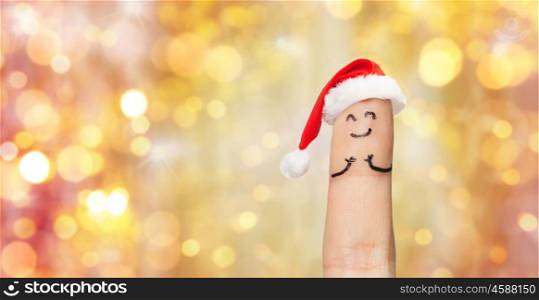 holidays, christmas and body parts concept - close up of one finger in santa hat over lights background