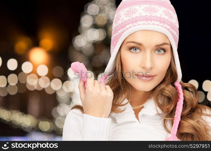 holidays, christmas and people concept - close up of young woman in winter hat over lights background. close up of woman in hat over christmas lights