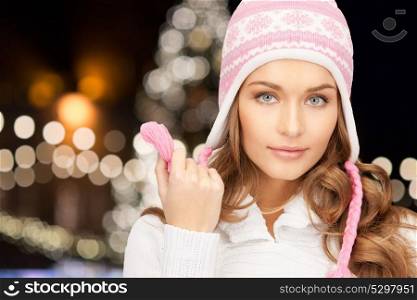 holidays, christmas and people concept - close up of young woman in winter hat over lights background. close up of woman in hat over christmas lights