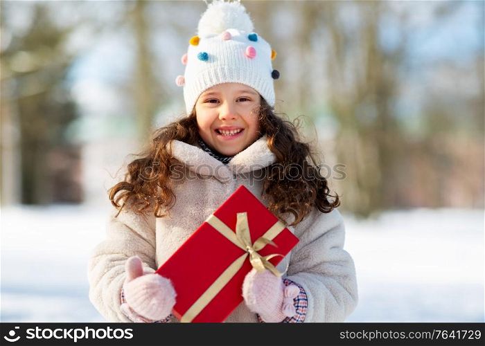 holidays, christmas and people concept - happy little girl with red gift box at winter park. happy girl with red christmas gift in winter park