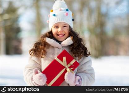 holidays, christmas and people concept - happy little girl with red gift box at winter park. happy girl with red christmas gift in winter park