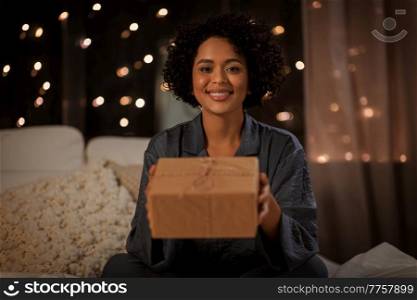 holidays, christmas and people concept - happy smiling woman in pajamas with gift box sitting in bed at night. woman in pajamas with gift sitting in bed at night