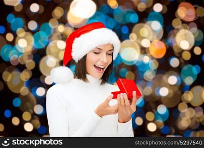 holidays, christmas and people concept - happy woman in santa hat opening gift box over lights background. happy woman in santa hat opening christmas gift
