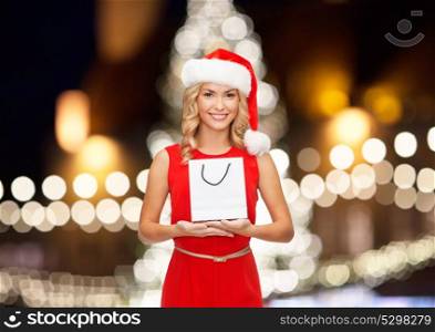 holidays, christmas and people concept - happy woman in santa hat with shopping bag over lights background. woman in christmas santa hat with shopping bag