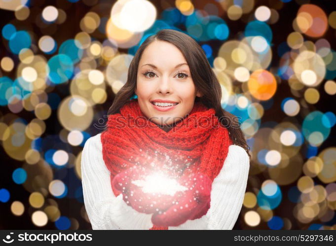 holidays, christmas and people concept - happy woman in scarf and mittens with magic snowflake over lights background. woman in scarf with christmas magic snowflake