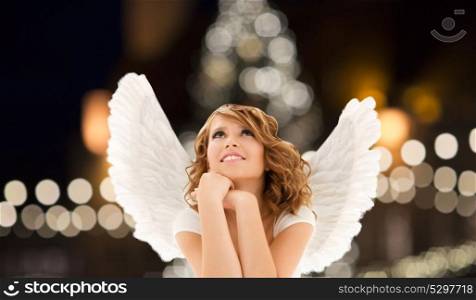 holidays, christmas and people concept - happy young woman or teenage girl with angel wings over lights background. happy woman with angel wings over christmas lights