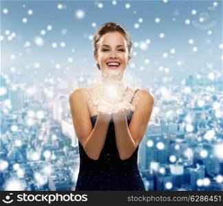 holidays, christmas and people concept - laughing woman in evening dress holding something over snowy city background