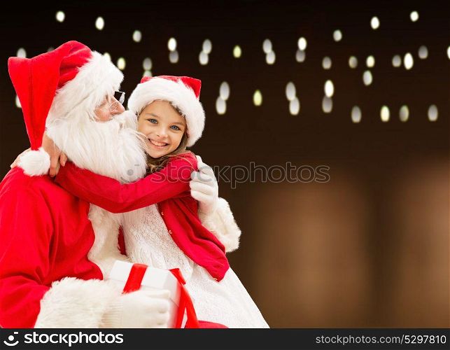 holidays, christmas and people concept - santa claus with gift and happy girl over lights background. santa claus with christmas gift and happy girl