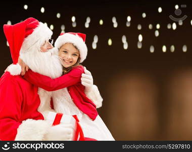 holidays, christmas and people concept - santa claus with gift and happy girl over lights background. santa claus with christmas gift and happy girl