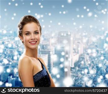 holidays, christmas and people concept - smiling woman in evening dress over snowy city background
