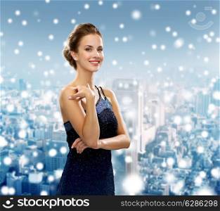 holidays, christmas and people concept - smiling woman in evening dress over snowy city background
