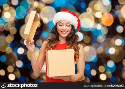 holidays, christmas and people concept - smiling woman in santa hat opening gift box over lights background. smiling woman in santa hat opening christmas gift