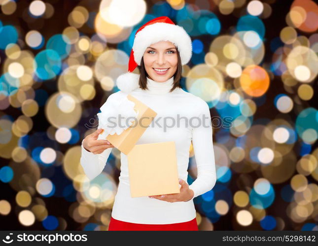 holidays, christmas and people concept - smiling woman in santa hat opening gift box over lights background. smiling woman in santa hat opening christmas gift