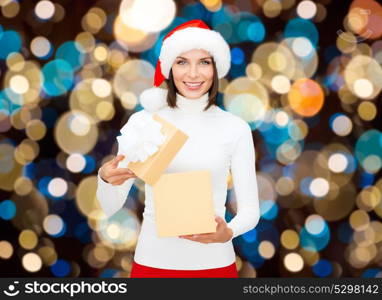 holidays, christmas and people concept - smiling woman in santa hat opening gift box over lights background. smiling woman in santa hat opening christmas gift