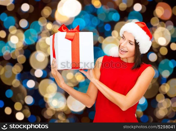 holidays, christmas and people concept - smiling woman in santa hat with gift box over lights background. smiling woman in santa hat with christmas gift