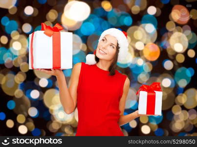 holidays, christmas and people concept - smiling woman in santa hat with gift boxes over lights background. smiling woman in santa hat with christmas gifts