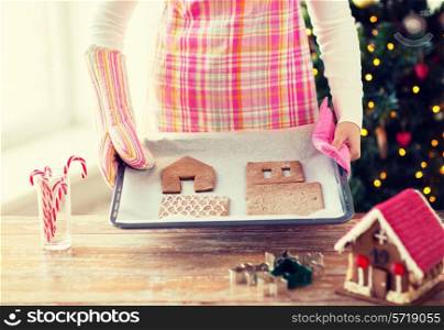 holidays, christmas, baking and sweets concept - closeup of woman holding pan with gingerbread house details on it at home