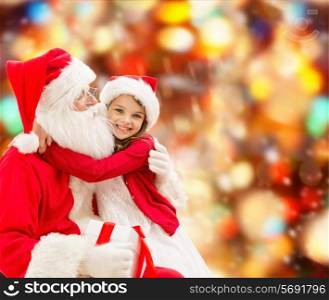 holidays, christmas, childhood and people concept - smiling little girl hugging with santa claus over red lights background