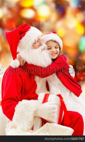 holidays, christmas, childhood and people concept - smiling little girl hugging with santa claus over red lights background