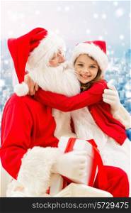 holidays, christmas, childhood and people concept - smiling little girl hugging with santa claus over snowy city background