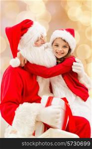 holidays, christmas, childhood and people concept - smiling little girl hugging with santa claus over beige lights background