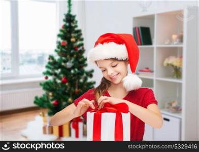 holidays, christmas, childhood and people concept - smiling little girl with gift box at home. smiling girl in santa hat with christmas gift