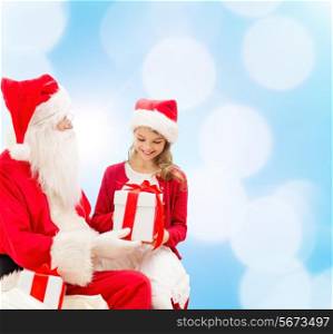 holidays, christmas, childhood and people concept - smiling little girl with santa claus and gifts over blue lights background