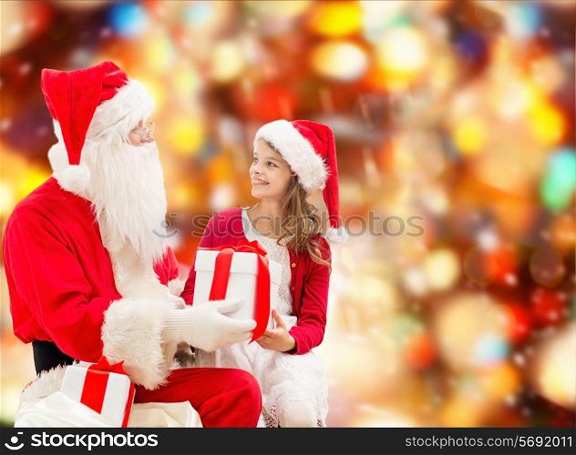 holidays, christmas, childhood and people concept - smiling little girl with santa claus and gifts over red lights background