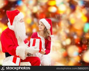 holidays, christmas, childhood and people concept - smiling little girl with santa claus and gifts over red lights background