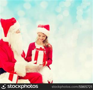 holidays, christmas, childhood and people concept - smiling little girl with santa claus and gifts over blue lights background