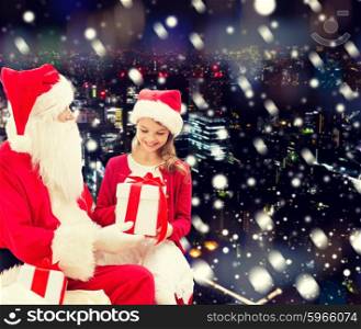 holidays, christmas, childhood and people concept - smiling little girl with santa claus and gifts over snowy city background