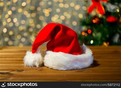 holidays, christmas, costume and tradition concept - close up of santa hat on wooden table over lights background