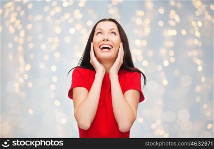 holidays, christmas, happiness, emotions and people concept - amazed laughing young woman in red dress over lights background