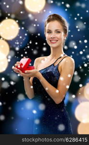 holidays, christmas, presents, luxury and people concept - smiling woman in dress holding red gift box night lights and snow background