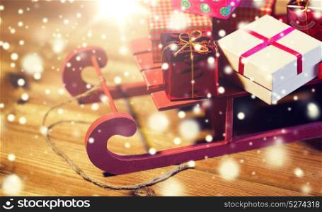 holidays, christmas, presents, new year and celebration concept - close up of many little gift boxes on red wooden sleigh on wooden table. close up of christmas gift boxes on wooden sleigh