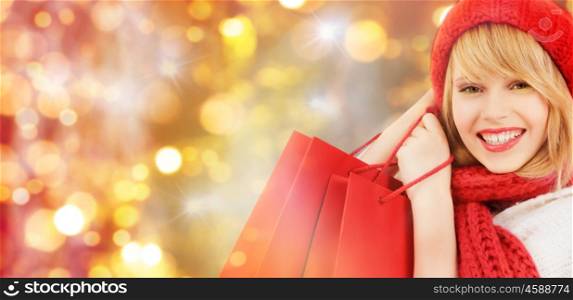 holidays, christmas, sale and people concept - close up of happy smiling young woman in winter clothes with shopping bags over lights background