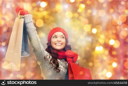 holidays, christmas, sale and people concept - happy smiling young asian woman in winter clothes with shopping bags over lights background